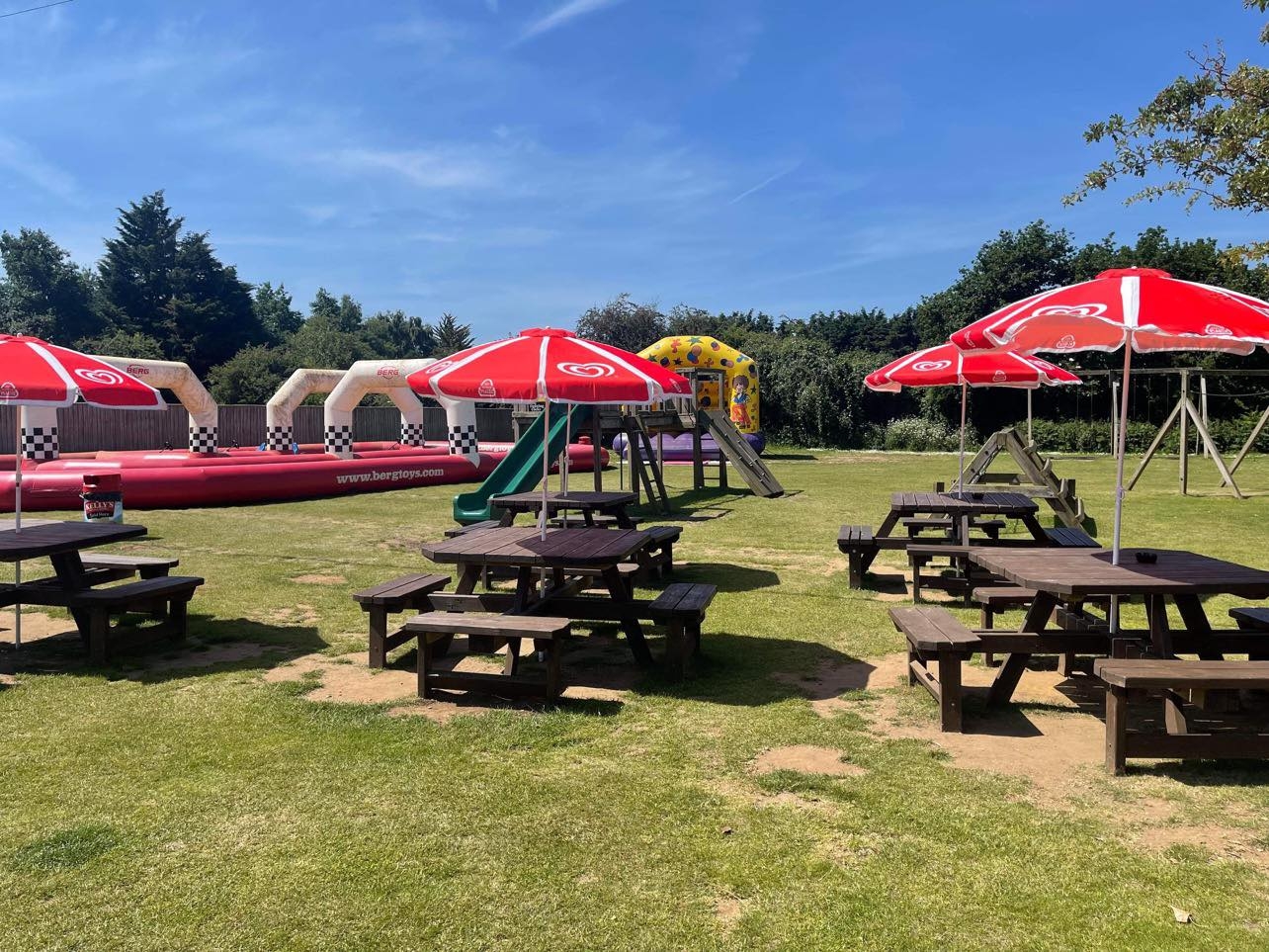 Beer garden with benches and umbrellas in the sun with bouncy castle in background