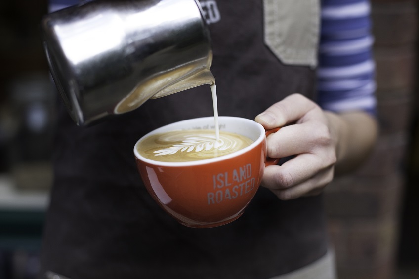 A barista pouring a milk leaf into a coffee