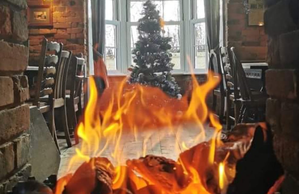 roaring open fire with Christmas tree and tables and chairs in the background
