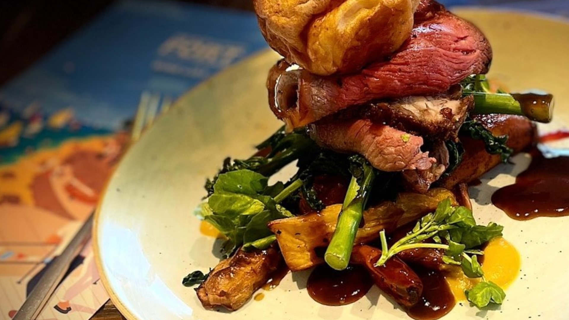 roast beef and yorkshire pudding on top of pile of roasted veg and potatoes