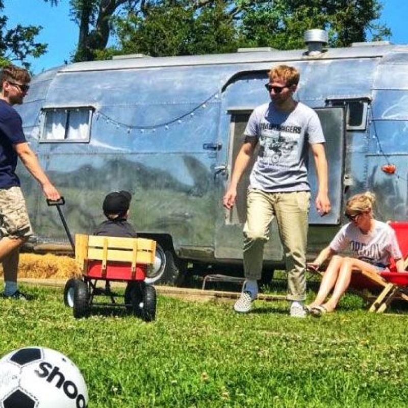 Airstream in a field with a family playing with a football 