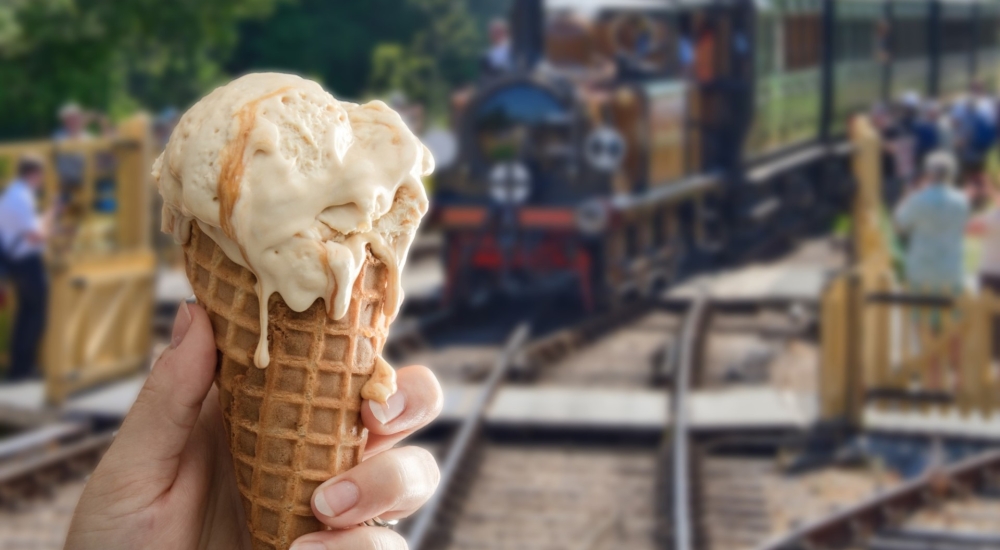 an ice cream cone held in one hand with a steam train in the background